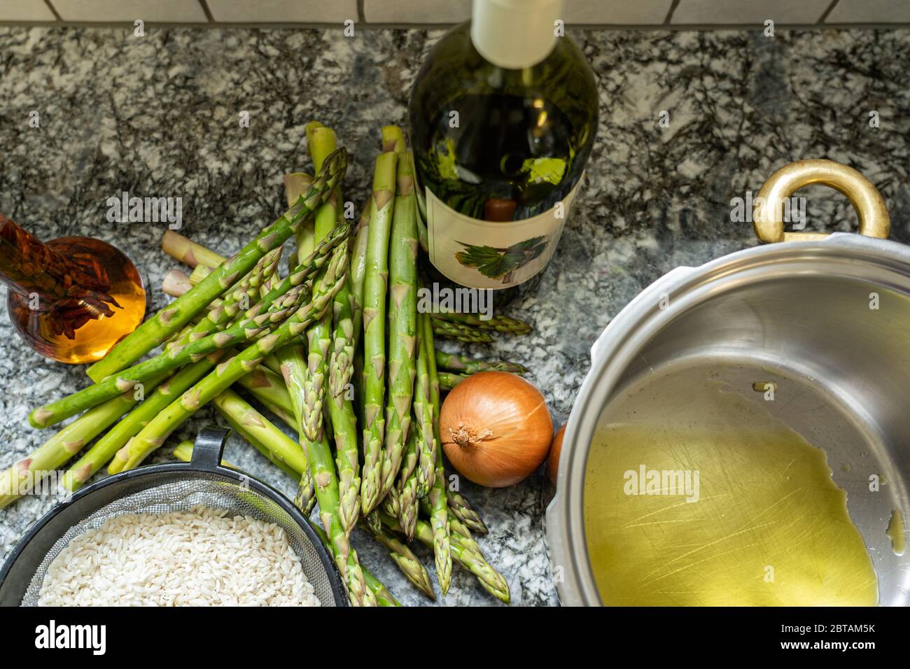 Risotto Reis mit Spargel, Zwiebeln und Weißwein kochen. Pfanne mit Olivenöl auf Granit Hintergrund. Hohe Winkelansicht. Stockfoto