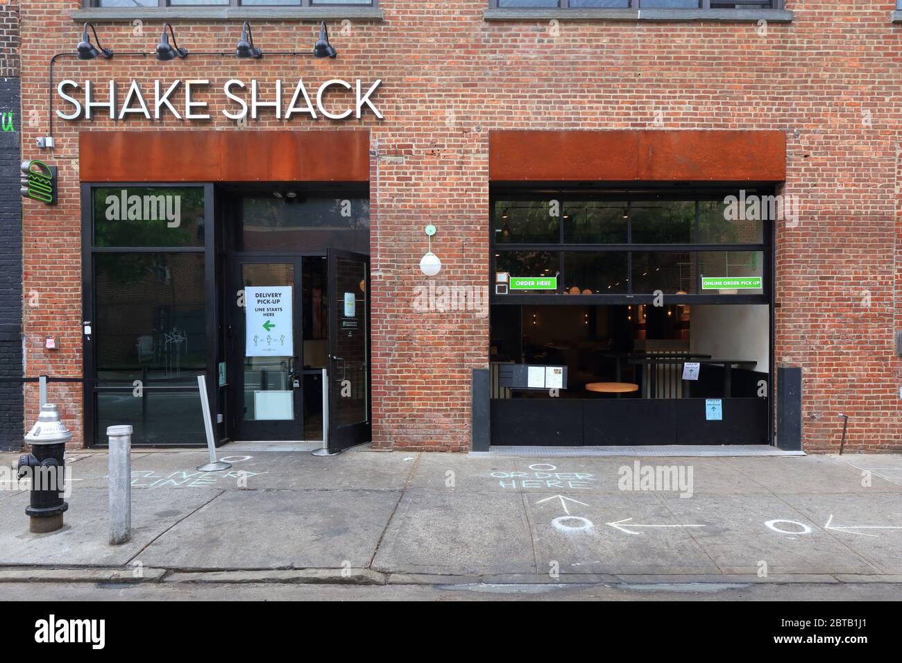 Eine Shake Shack in Brooklyns Stadtteil Williamsburg mit sozialen Distanzkreisen in Kreide und separaten Abholungs-, Liefer- und Bestellfenstern Stockfoto