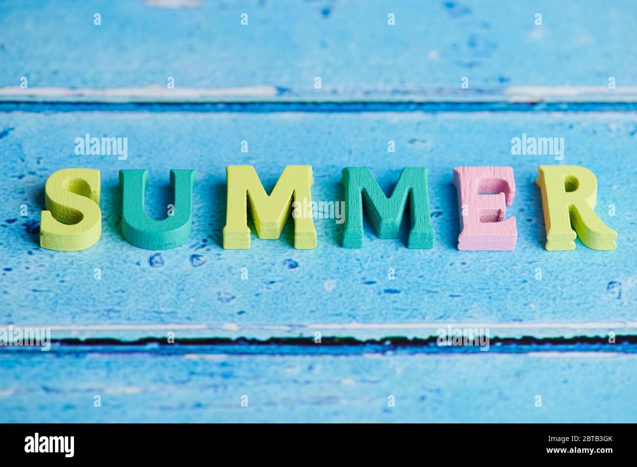Das Wort Sommer legte mit farbigen hölzernen Buchstaben auf blauem Hintergrund mit Kopierraum Stockfoto