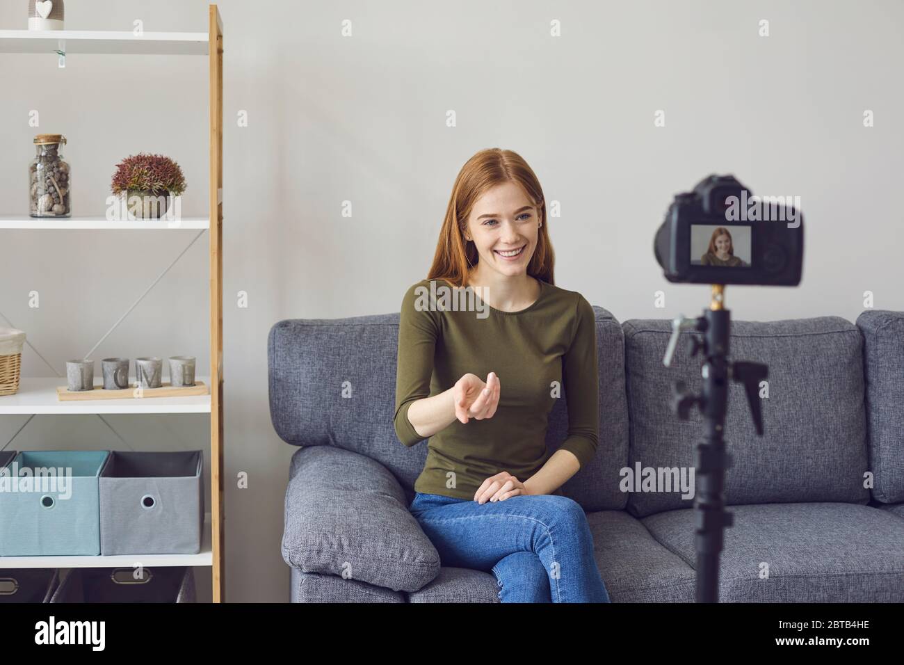 Blogger Vlogger Mädchen spricht mit der Kamera, während auf einem Sofa in einem Raum zu Hause sitzen. Ein junges Mädchen spricht gestikulierend mit seinen Händen drinnen. Stockfoto