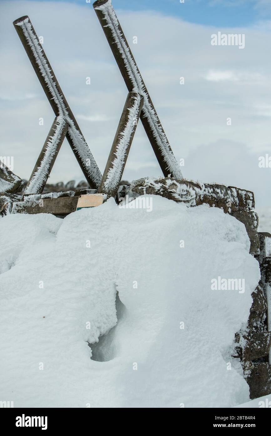 Ein Holzstollen über einer trockenen Steinmauer, die im Winter mit Schnee und Eis bedeckt ist, Yorkshire Dales National Park, Großbritannien Stockfoto