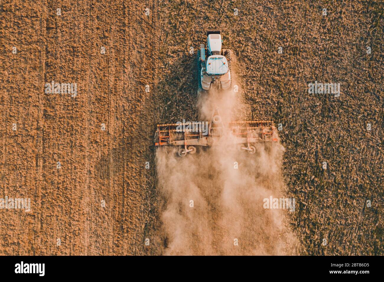 Oben ein Feld fliegen auf einer Drohne während der Aussaat im Frühjahr, wenn ein Raupentraktor mahlt den Boden mit einem Grubber in Zeiten der wirtschaftlichen cri Stockfoto