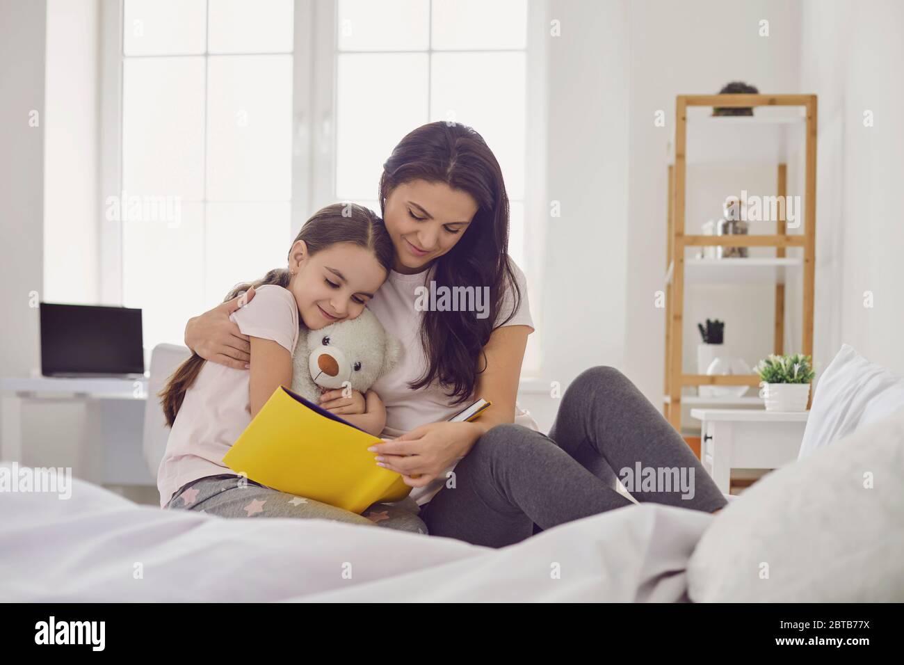 Alles Liebe zum Muttertag. Mutter und Tochter lesen ein Buch, während sie zu Hause auf dem Bett sitzen. Mama liest ihrem Kind in einem Buch bef eine interessante Geschichte vor Stockfoto