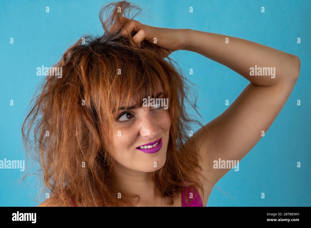 Besorgte junge Frau mit krauses rotes Haar kratzt ihre Kopfhaut Stockfoto