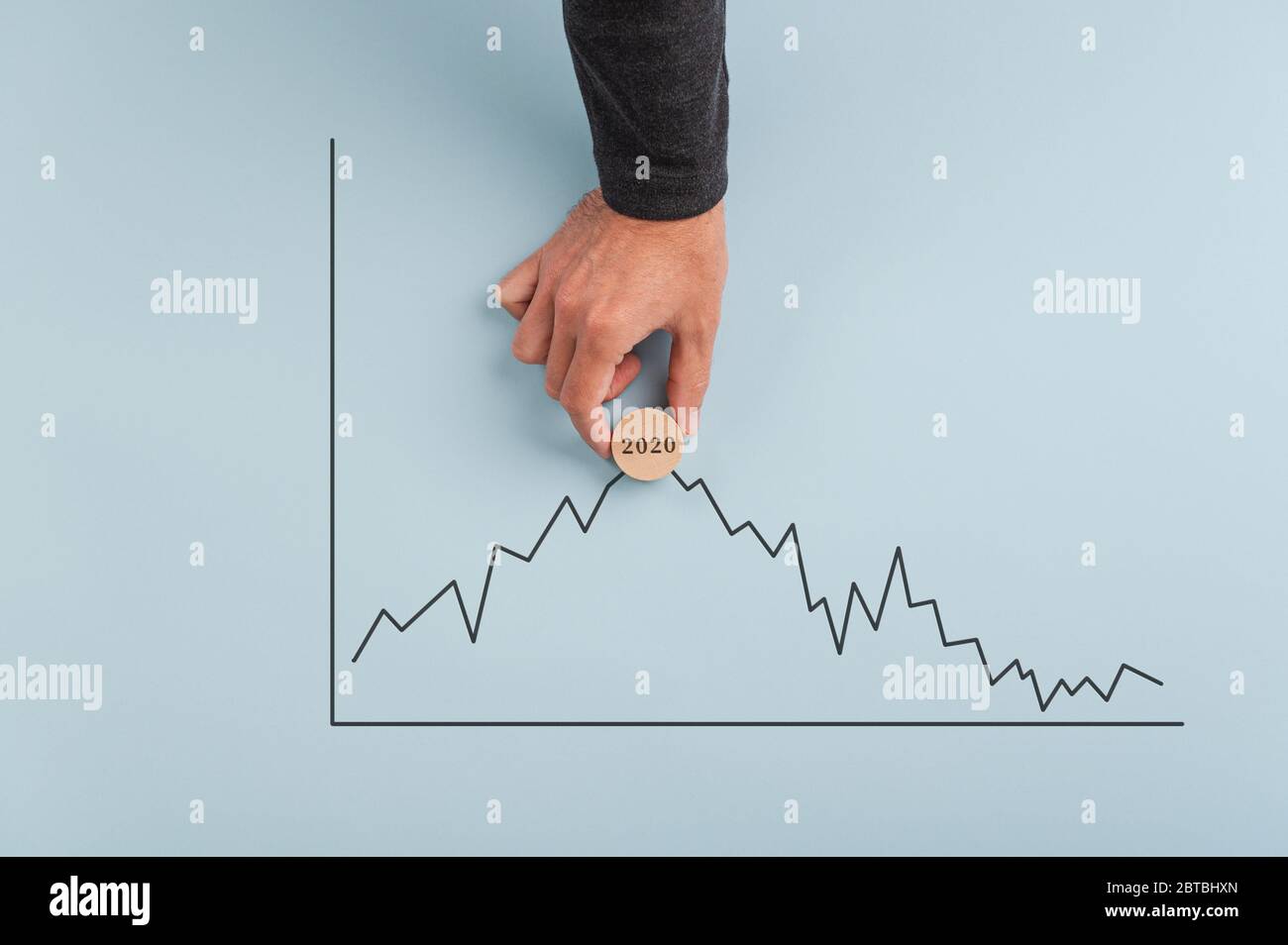 Männliche Hand, die einen hölzernen Schnittkreis mit 2020 Zeichen auf sie auf einem statistischen Diagramm gerade vor einem Rückgang setzt, eine Börsenkrise vorhersagend. Stockfoto