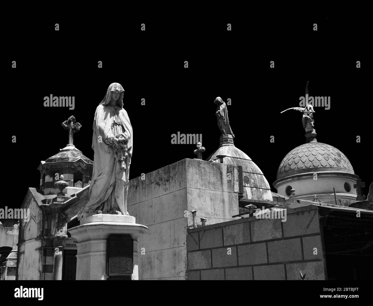 Einige religiöse Statuen in Gräbern auf einem Friedhof unter einem schwarzen Himmel in Buenos Aires in Argentinien Stockfoto