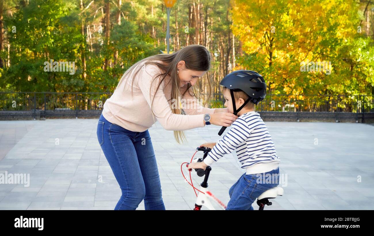 Schöne lächelnde Frau Anpassung und Befestigung Helmschnalle auf ihrem Sohn Kopf Reiten ein Fahrrad Stockfoto