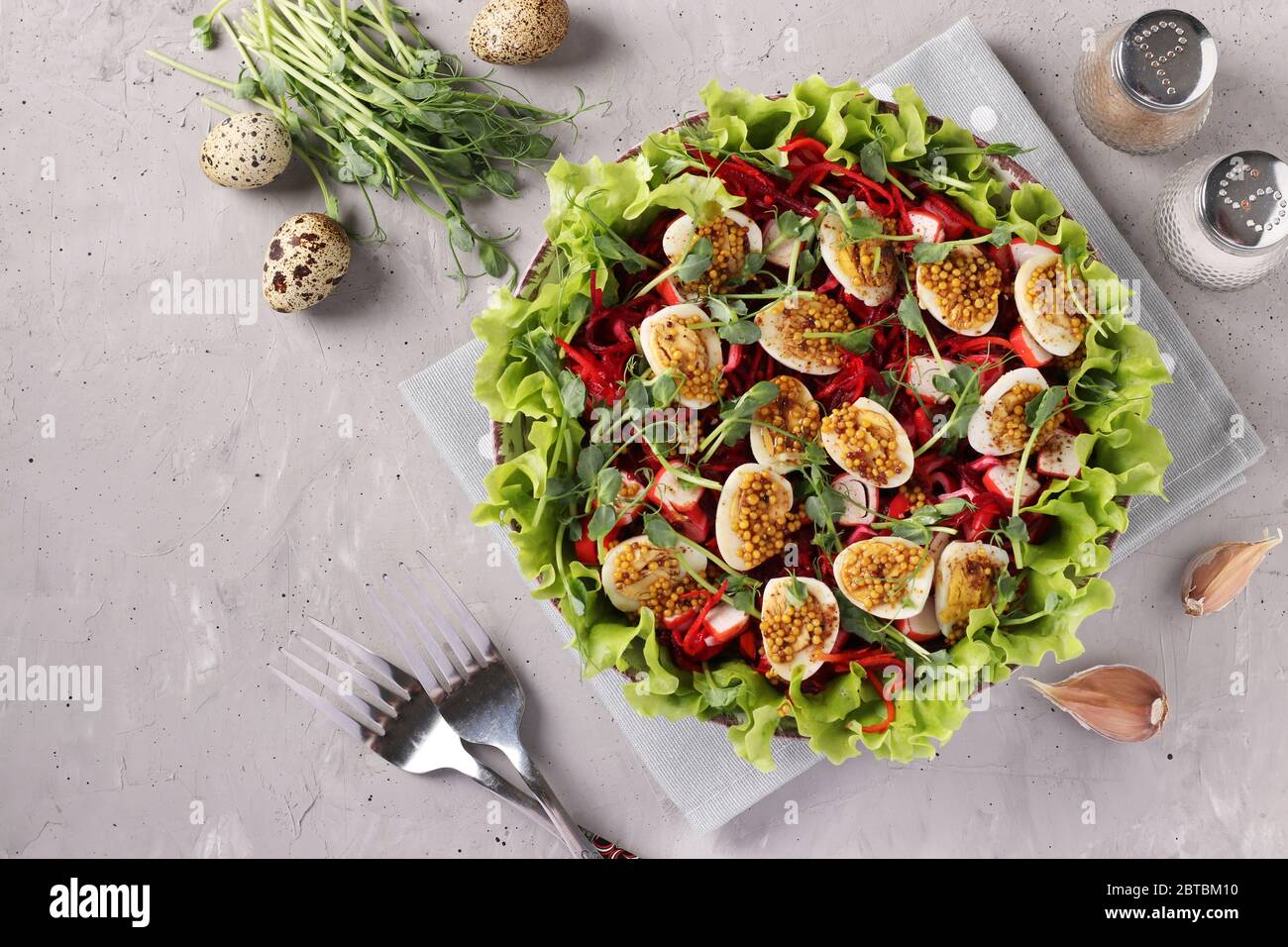 Salat aus Bio-Salatblättern, Erbsen, Mikrogrün, Karotten, Rote Bete und Wachteleier, gewürzt mit Senf und Olivenöl auf hellgrauem Hintergrund Stockfoto