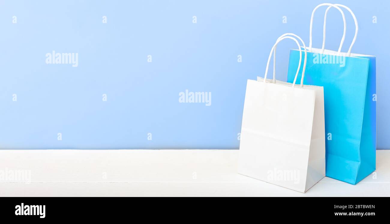 Weiße blaue Handarbeitspapiertaschen. Shopping Mockup Taschen Papier-Pakete auf weißem Tisch blaues Licht Hintergrund mit Kopierraum. Einkaufen, Verkauf, Lieferung von Lebensmitteln Stockfoto