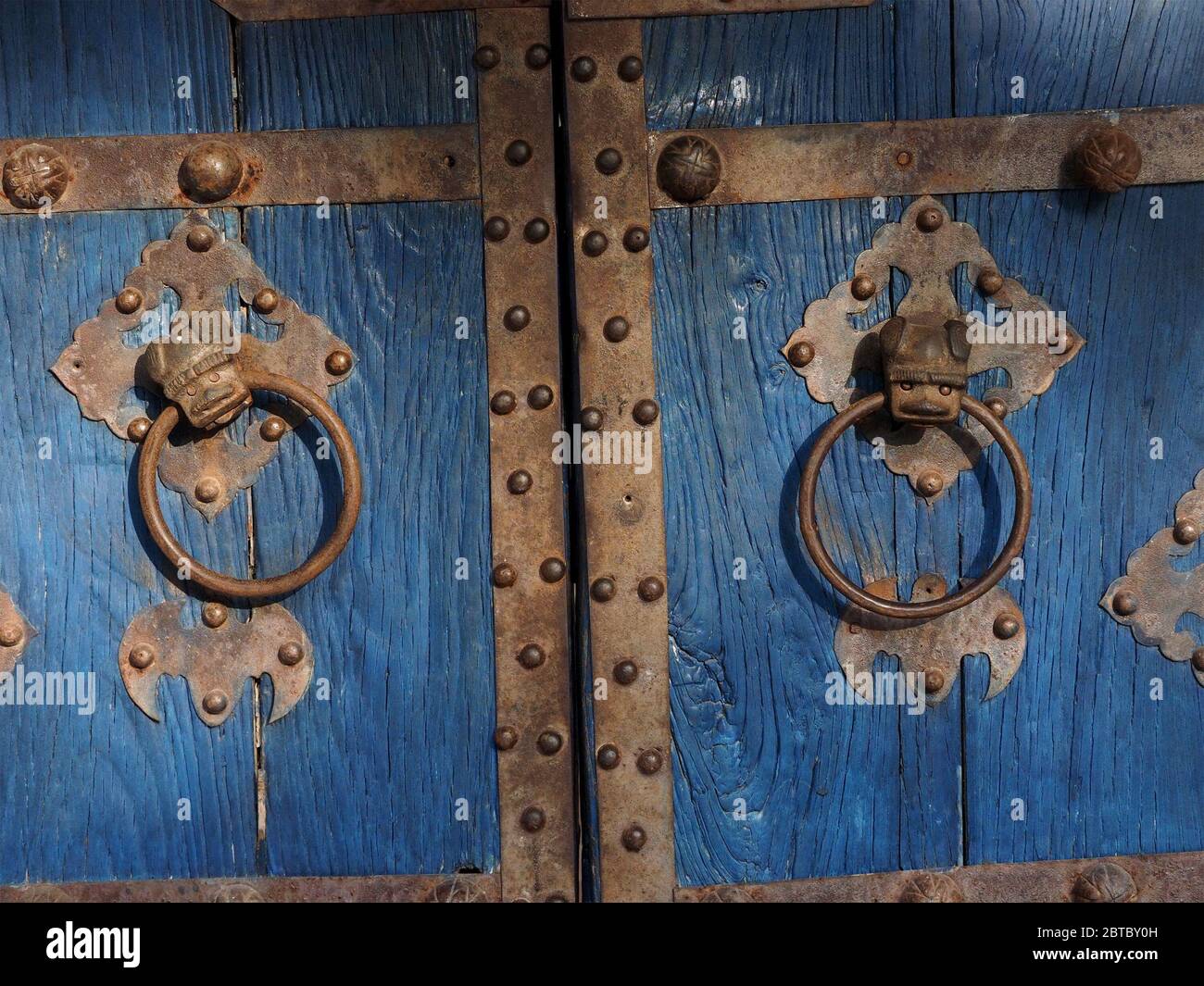 Detail von primitiven Gesicht Designs auf Metall Tür Klopfer auf blau lackiert traditionelle Doppeltür mit besetzt Metallarbeiten in Malindi, Kenia Küste, Afrika Stockfoto