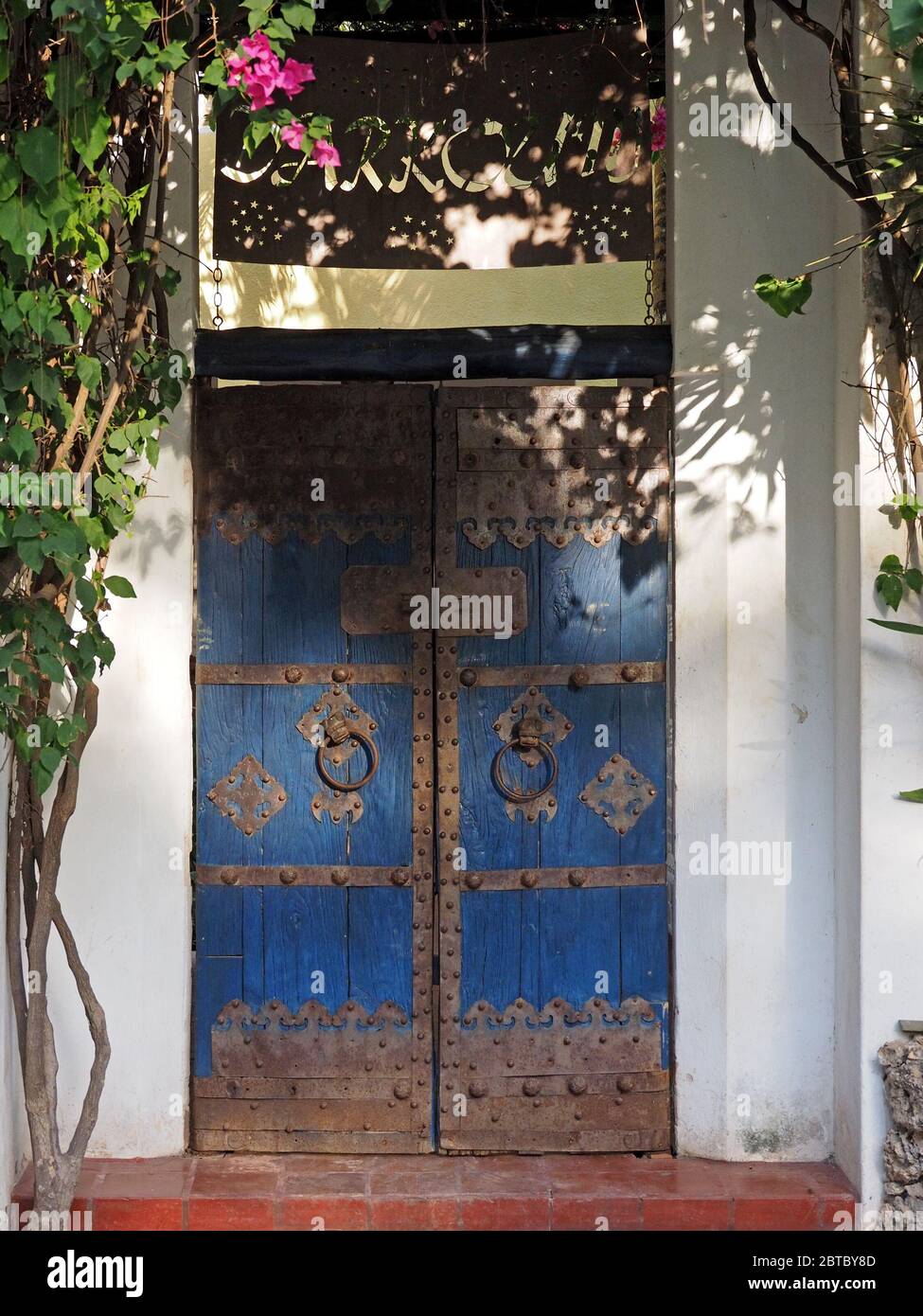 Rostige Metallarbeiten und Türklopfringe auf blau lackierten traditionellen Holz Doppeltür in weiß lackiertem Gebäude in Malindi, an der Küste Kenias, Afrika Stockfoto