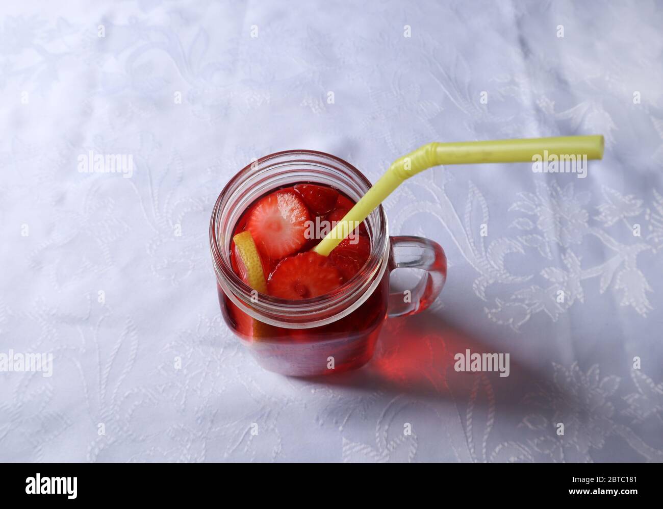 Erdbeer-Smoothie in Scheiben geschnitten und eine Scheibe Zitrone in einem Glasgefäß und einem Trinkschlauch in einem Glas auf einem Schreibtisch zu Hause Stockfoto