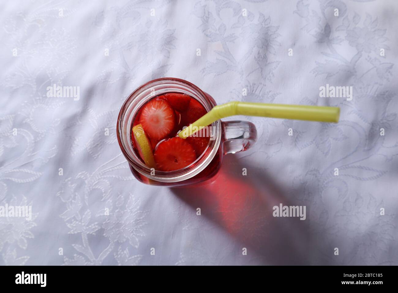 Erdbeer-Smoothie in Scheiben geschnitten und eine Scheibe Zitrone in einem Glas mit einem Trinkschlauch auf einem Schreibtisch zu Hause dekoriert. Sommer- und Saisonessen Stockfoto