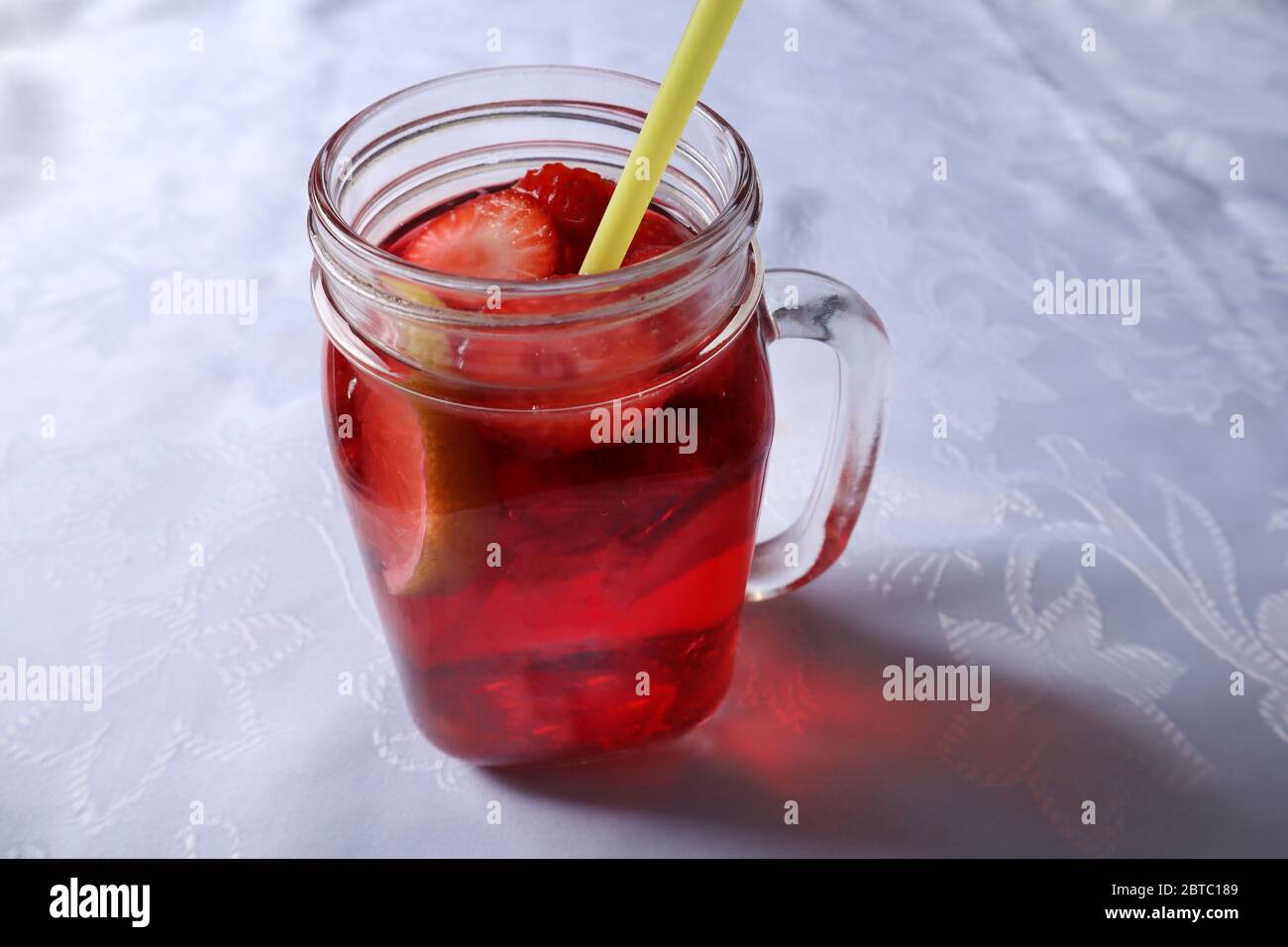 Erdbeer-Smoothie in Scheiben geschnitten und eine Scheibe Zitrone in einem Glas mit einem Trinkschlauch auf einem Schreibtisch zu Hause dekoriert. Sommer- und Saisonessen Stockfoto