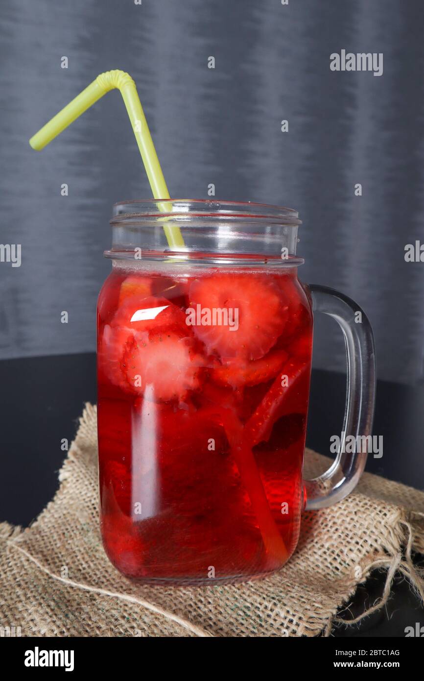 Erdbeer-Smoothie-Drink in einem Glas mit einem Trinkschlauch auf einem Schreibtisch zu Hause dekoriert. Sommer und Saison Essen und Trinken Konzept Stockfoto
