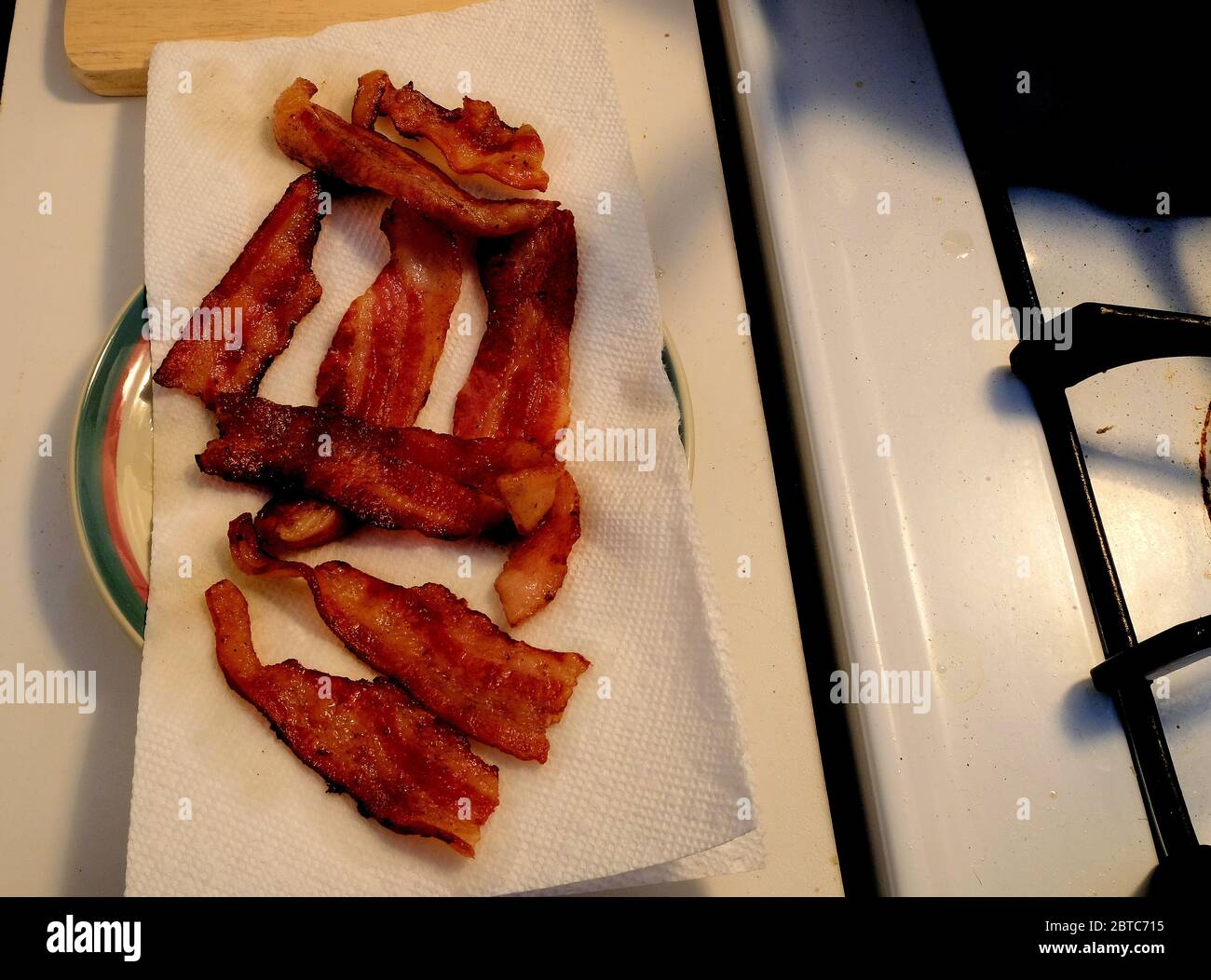 Gekochter Speck Streifen auf einem weißen Papiertuch an einem Herd; Speck sickerte Fett von einem Papiertuch absorbiert. Stockfoto