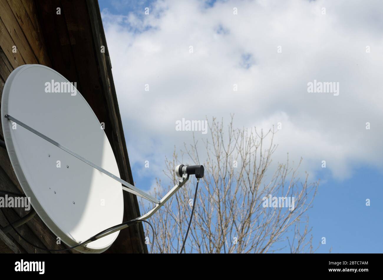 Satellitenschüssel auf einem Landhaus auf einem Hintergrund eines blauen Himmels mit Wolken. Die Bedeutung der Telekommunikation in der Zeit der Selbstisolierung. Stockfoto