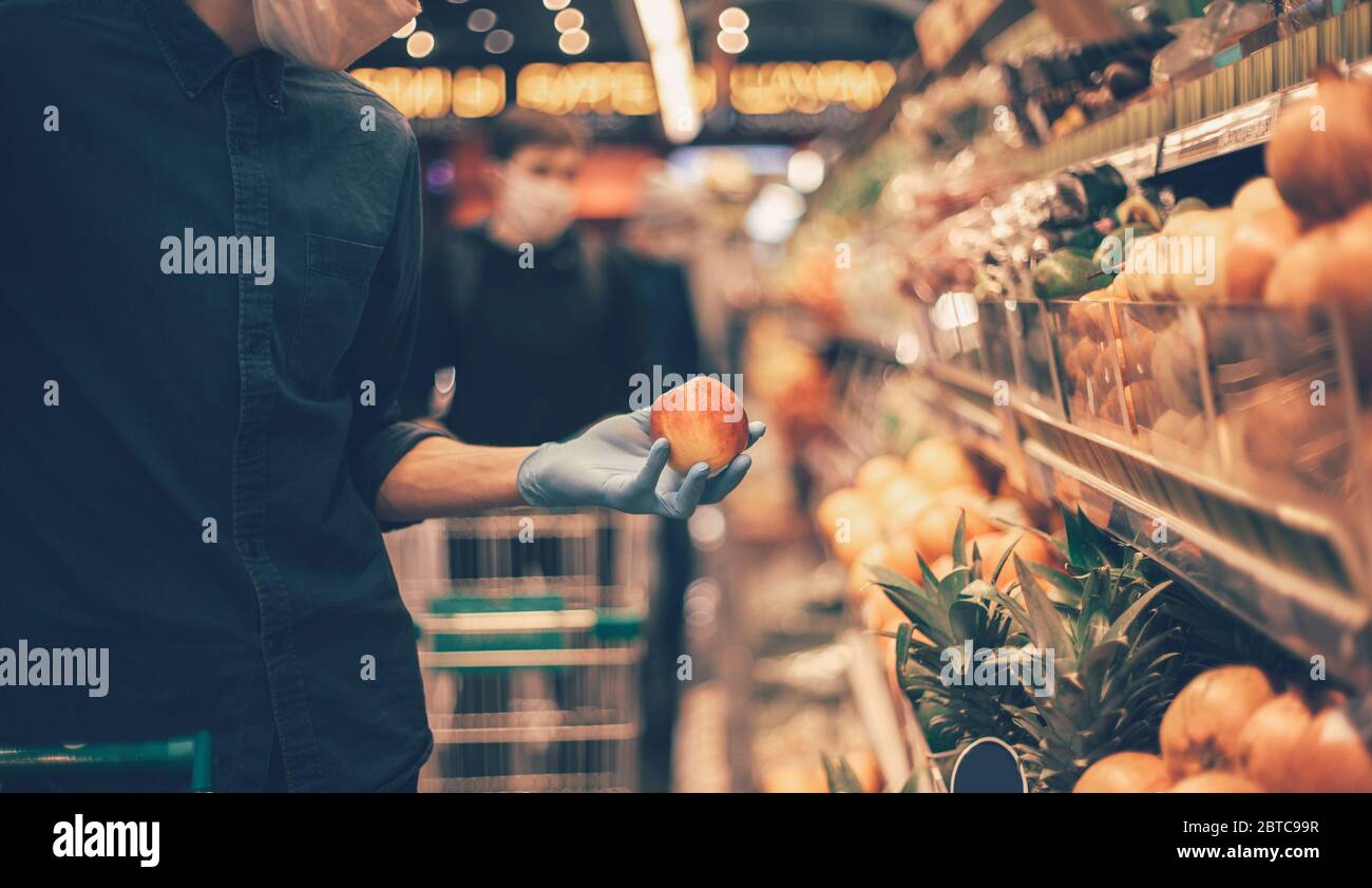 Mann in einer Schutzmaske bei der Auswahl von Äpfeln im Supermarkt. Stockfoto