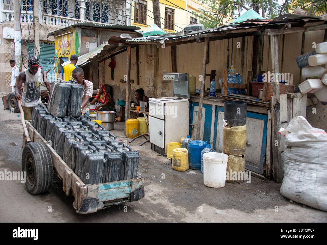 Straßenszene in Mombasa, die das Leben auf der Straße zeigt, und Männer, die den Wagen mit großen Plastikkannen schieben, die Wasser zum Verkauf tragen Stockfoto