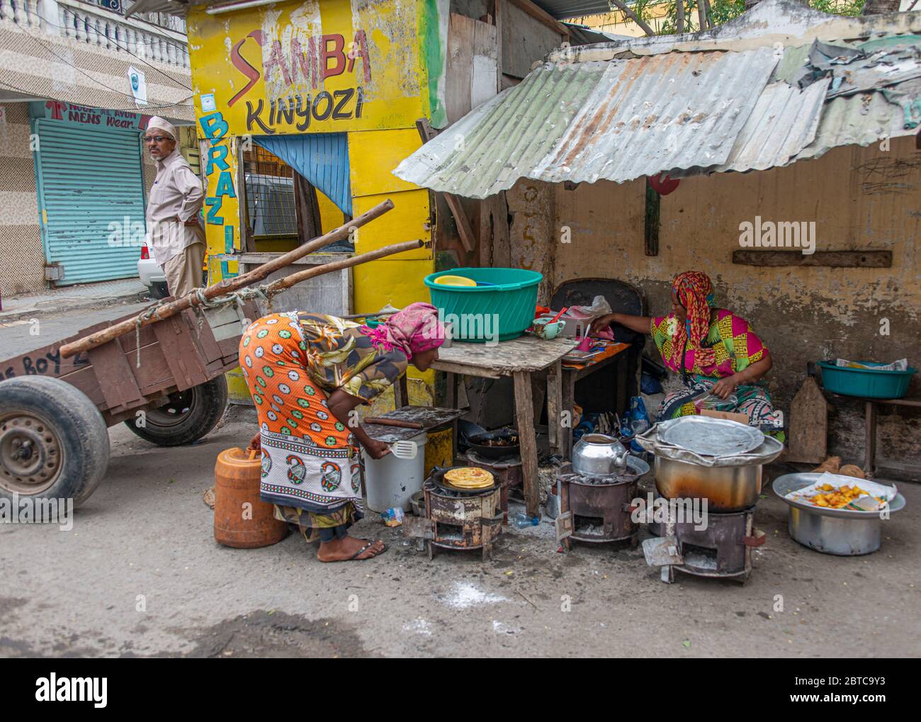 Straßenszene in Mombasa, die das Leben auf der Straße zeigt und Frauen, die Lebensmittel zum Verkauf kochen Stockfoto