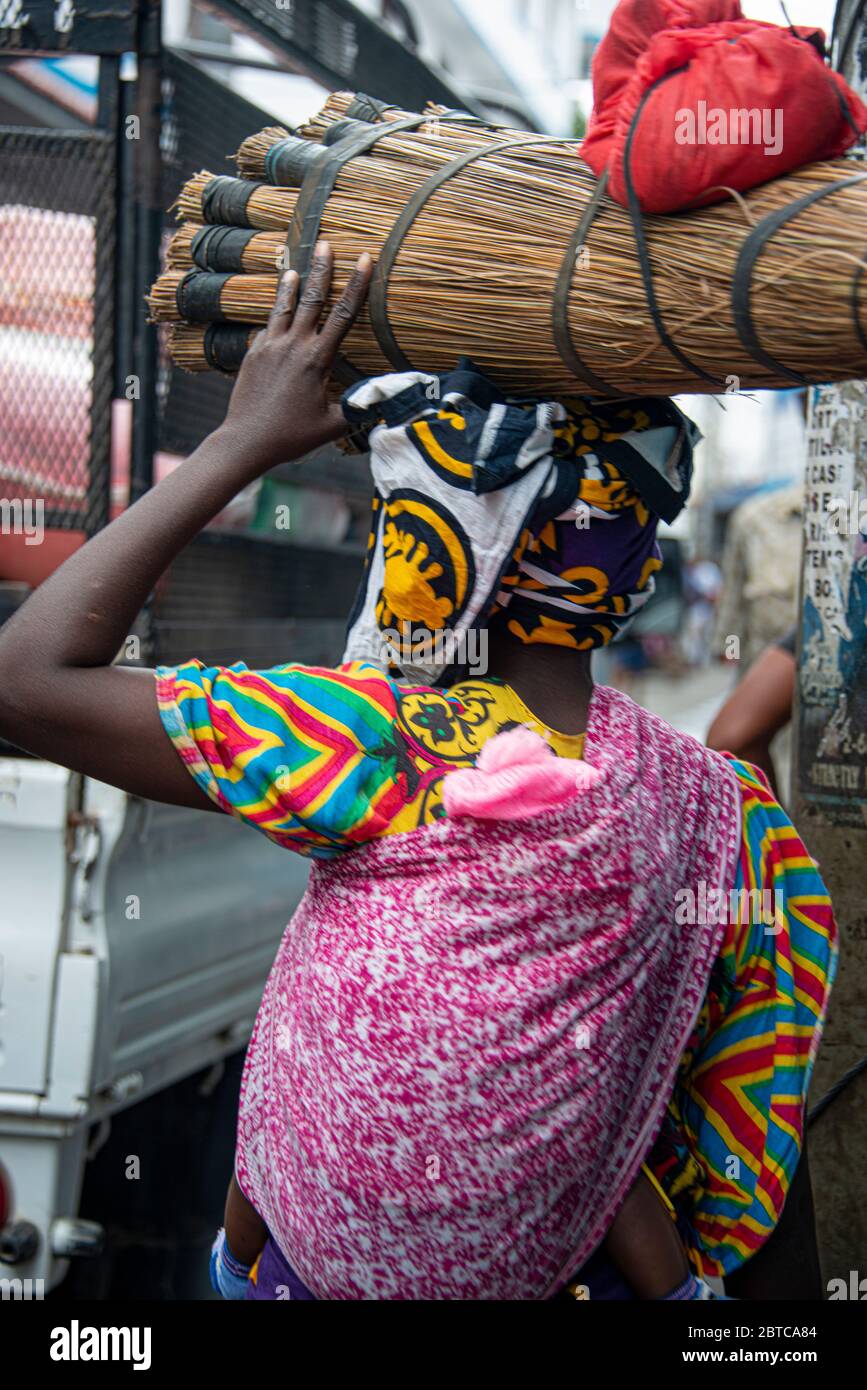 Frau mit Besen auf dem Kopf und Baby auf dem Rücken in Mombasa Stockfoto