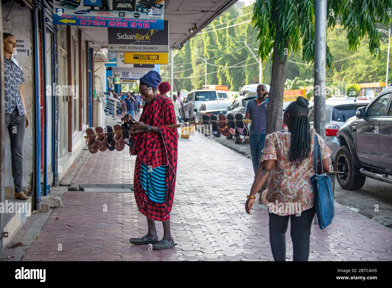 Mann, der Schuhe auf einer Straße in Mombassa verkauft und auf sein Telefon schaut Stockfoto