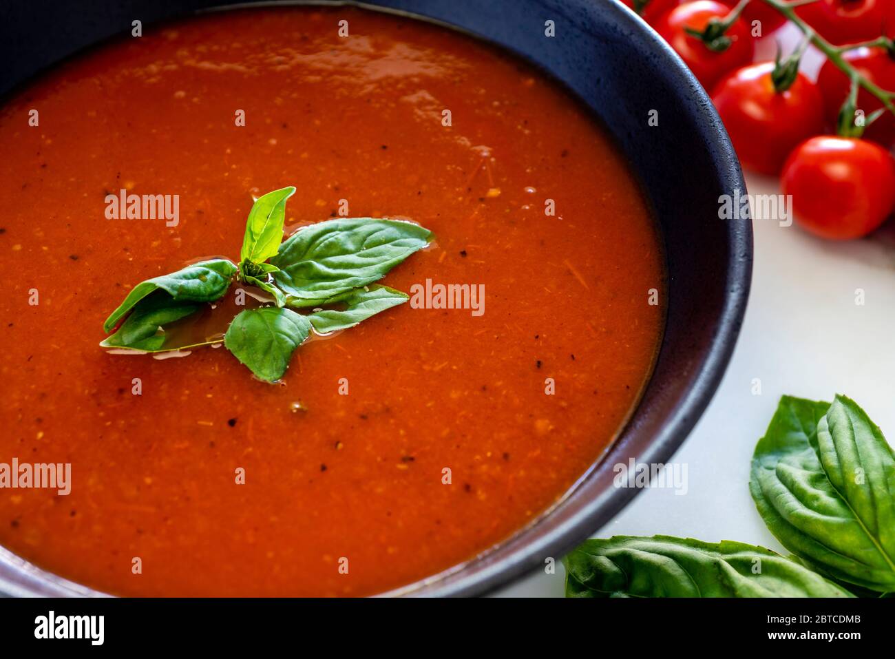 Tomatensuppe in dunkler Schüssel mit Basilikumgarnitur Stockfoto