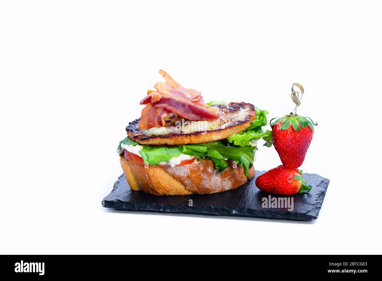 Nahaufnahme eines köstlichen offenen Sandwich mit verschiedenen Fleisch, Gemüse und Käse neben frischen Erdbeeren auf einem dunklen Teller auf hellem Hintergrund. spani Stockfoto