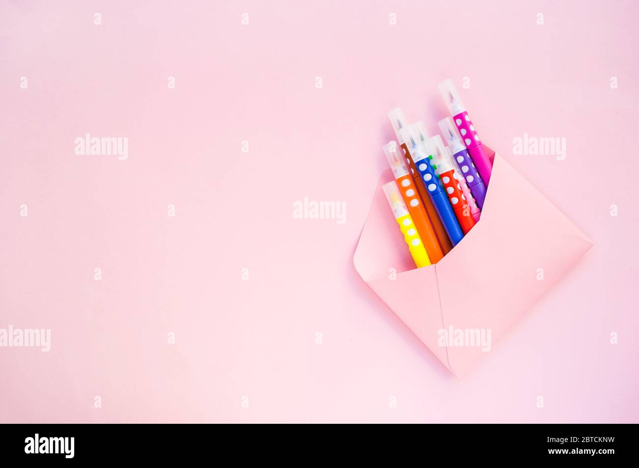 Papier rosa Umschlag voller bunten Marker auf pastellrosa Hintergrund mit Copyspace. Stockfoto