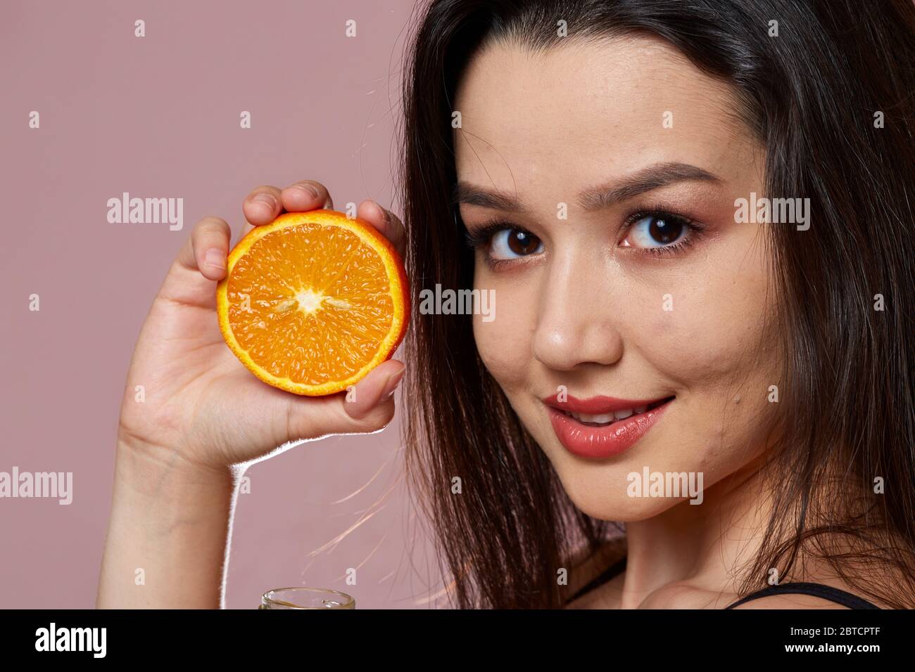 Junge schöne schlanke asiatische Mädchen in einem Badeanzug. Halten einer Orange. Lächeln. Auf einem rosa isolierten Hintergrund. Stockfoto