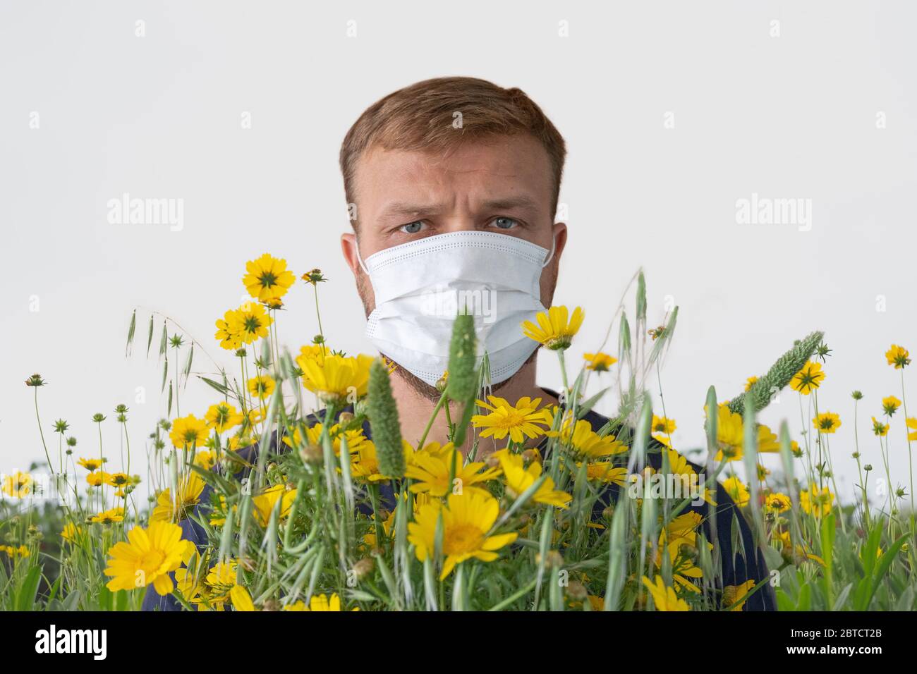 Europäischer Mann, der auf einem blühenden Feld in einer medizinischen Gesichtsmaske steht. Konzept einer saisonalen Allergien Stockfoto