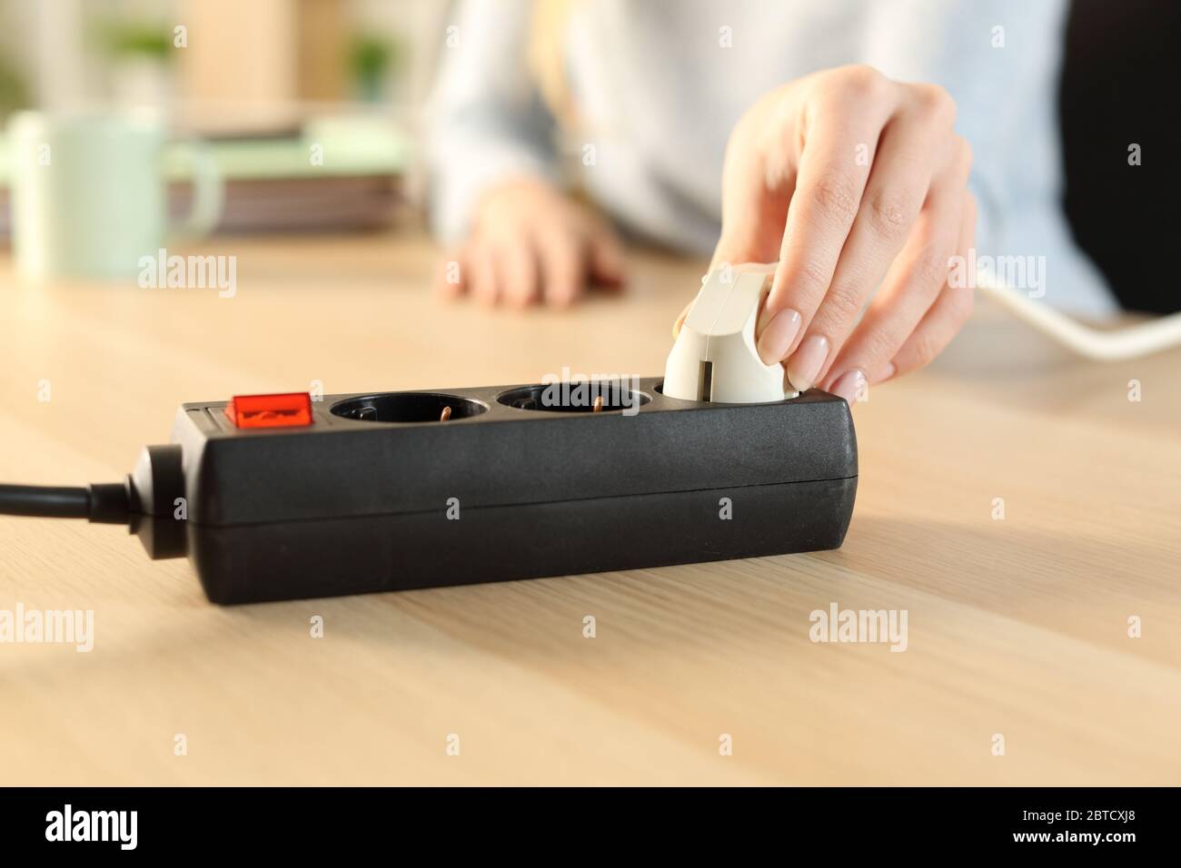 Nahaufnahme einer Frau, die zu Hause einen Stecker an eine Steckdosenleiste ansteckt Stockfoto