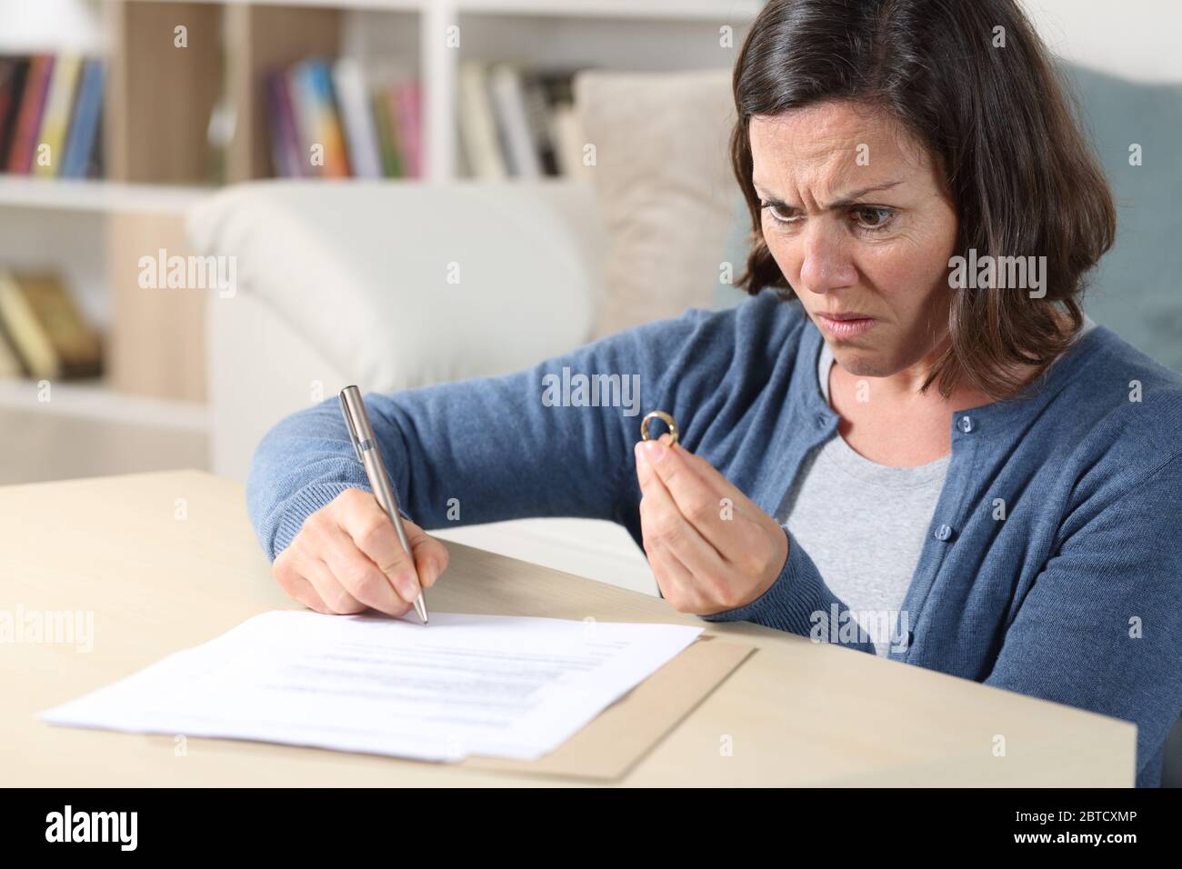 Wütend Frau Unterzeichnung Scheidung Papiere Blick auf Ehering sitzt auf dem Boden im Wohnzimmer zu Hause Stockfoto