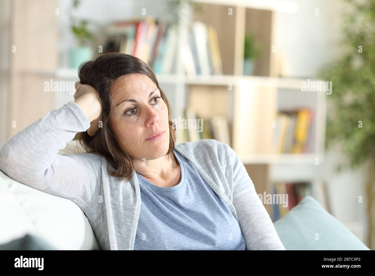 Nachdenkliche Erwachsene Frau, die denkt, wegschauen und zu Hause auf der Couch sitzen Stockfoto