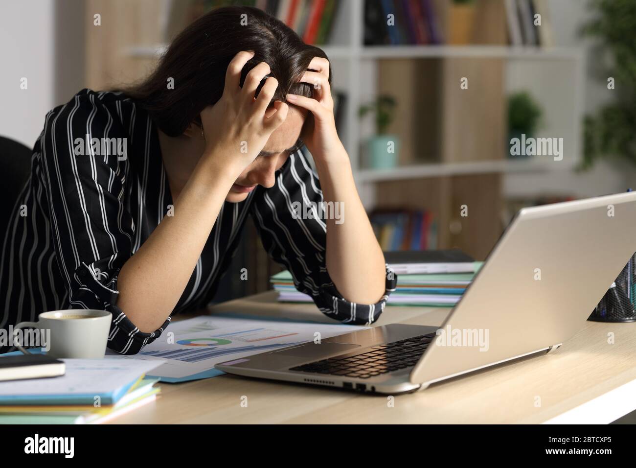Traurige Unternehmerin mit Laptop, die sich beschwert, nachts zu Hause auf einem Schreibtisch zu sitzen Stockfoto