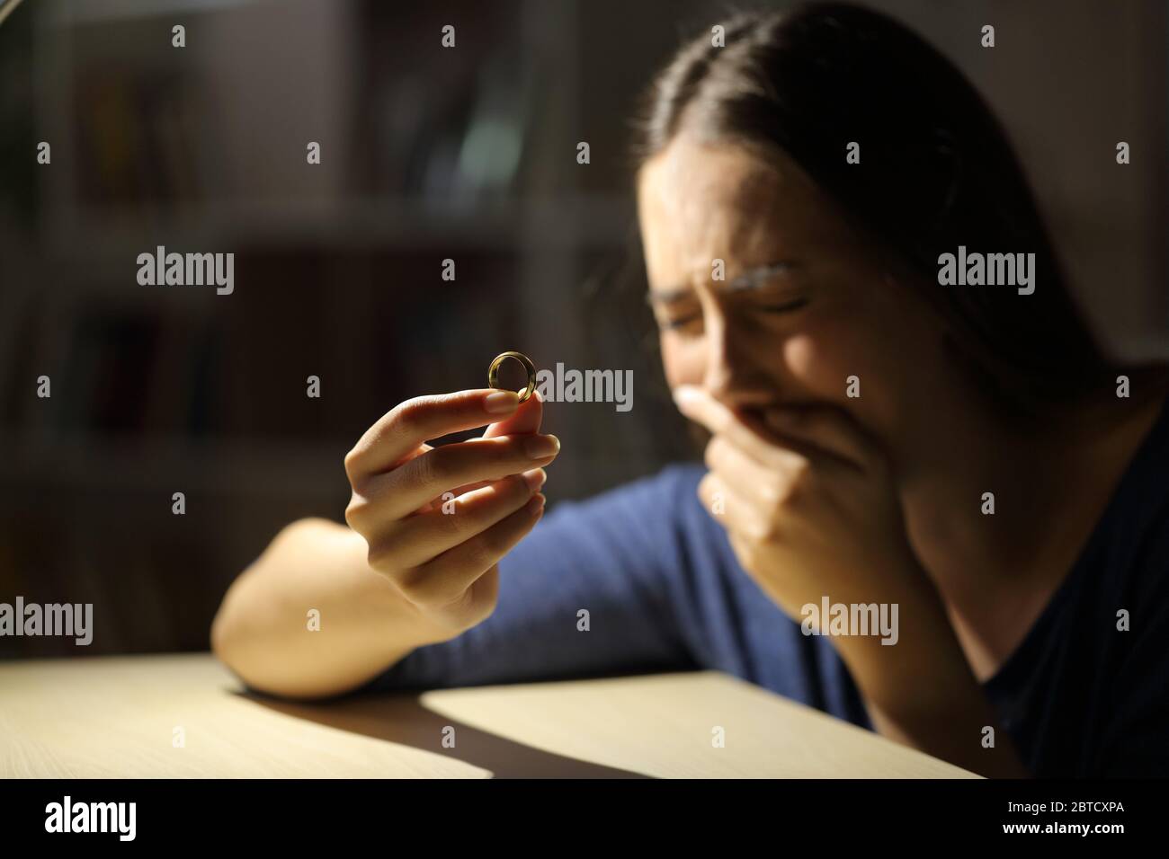 Traurige Frau weinend einen Ehering haltend beschwerend allein in der Nacht zu Hause sitzen Stockfoto