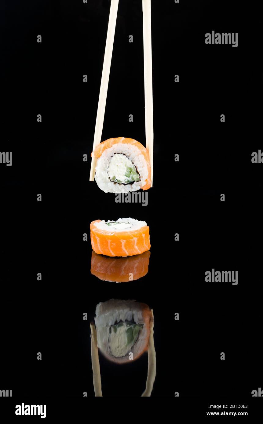 Essstäbchen, die Sushi philadelphia mit Lachs auf schwarzem Hintergrund einnehmen. Asiatische Restaurantkarte. Vorlage Mockup, Platz für Text. . Stockfoto