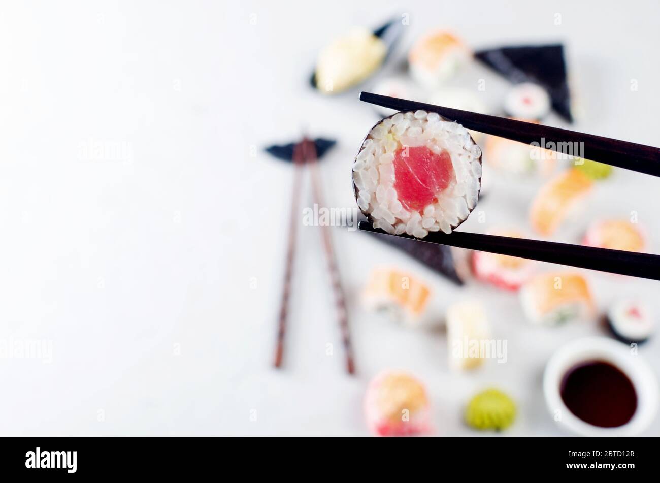 Nahaufnahme der Essstäbchen, die eine Portion Sushi-Rolle über dem Tisch mit verschiedenen Sushi, Sojasauce, Ingwer, Wasabi einnehmen. Sushi-Menü. Lieferservice Japanisch Stockfoto