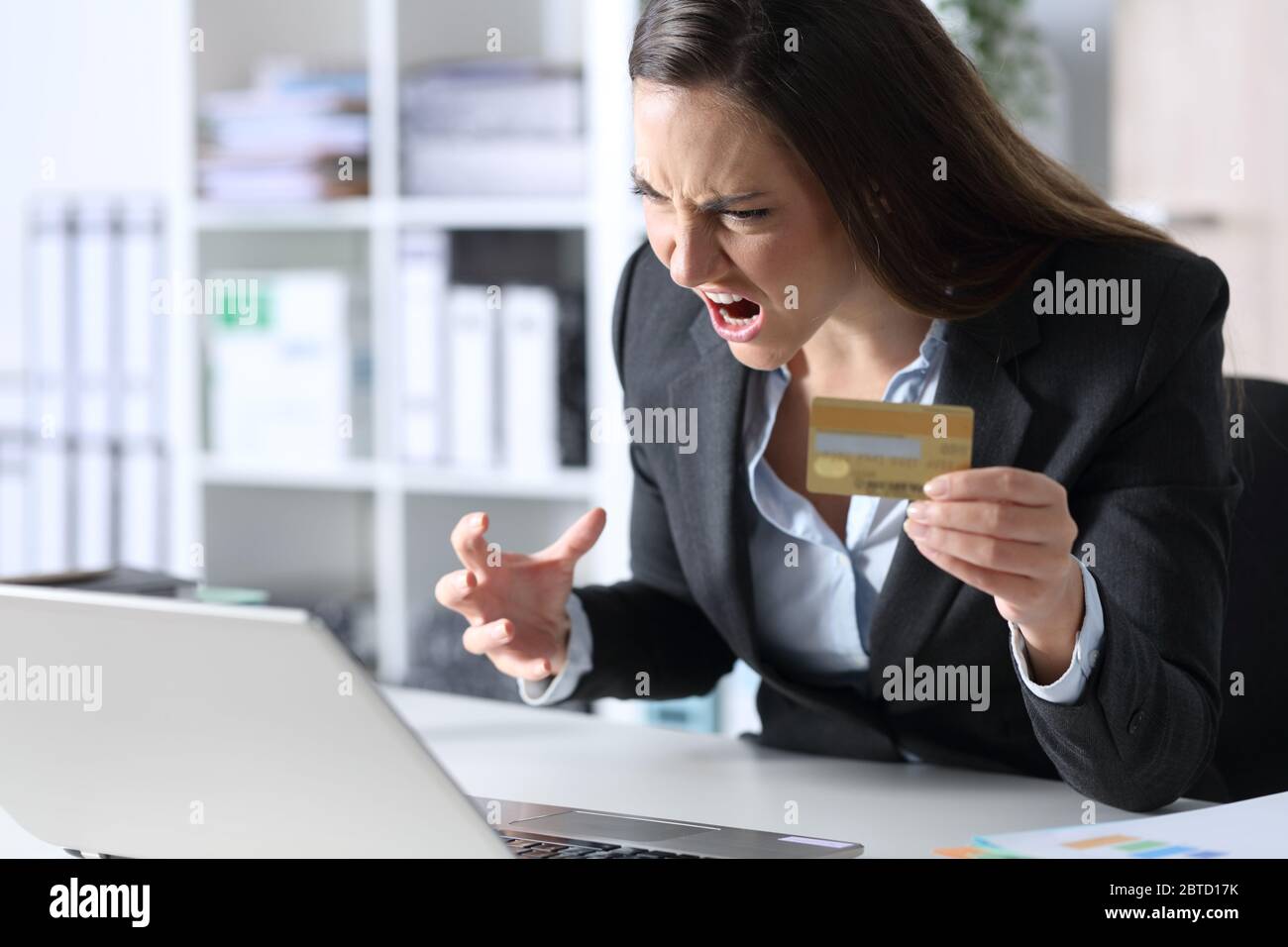 Wütende Exekutive Frau zahlt online mit Kreditkarte auf Laptop sitzt auf einem Schreibtisch im Büro Stockfoto