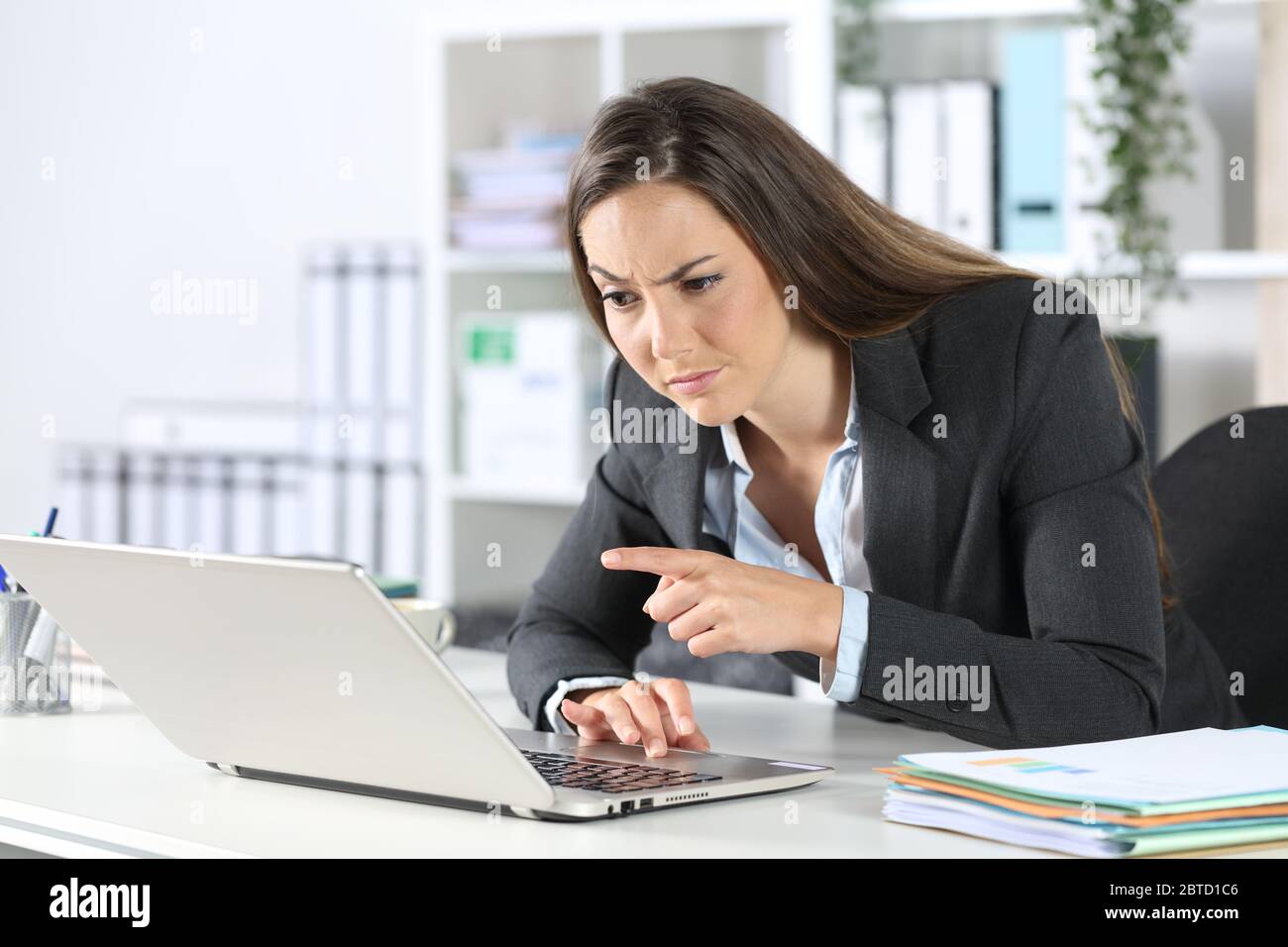 Verdächtige Führungskraft, die auf einem Laptop auf einem Schreibtisch im Büro sitzt und liest Stockfoto