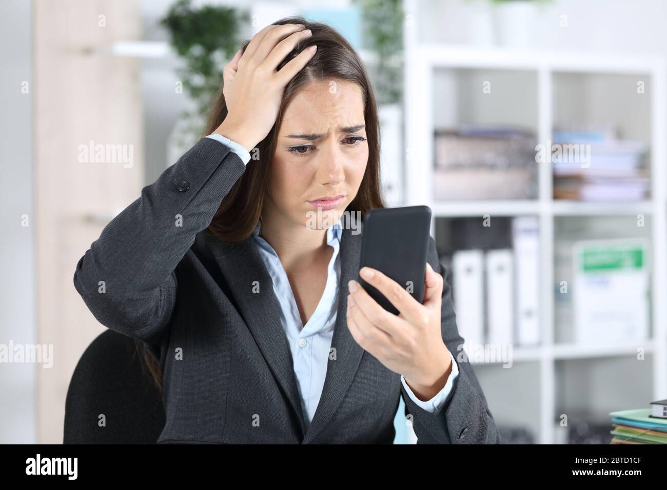 Traurig besorgte Exekutive Frau entdeckt Fehler auf Smartphone sitzt auf einem Schreibtisch im Büro Stockfoto
