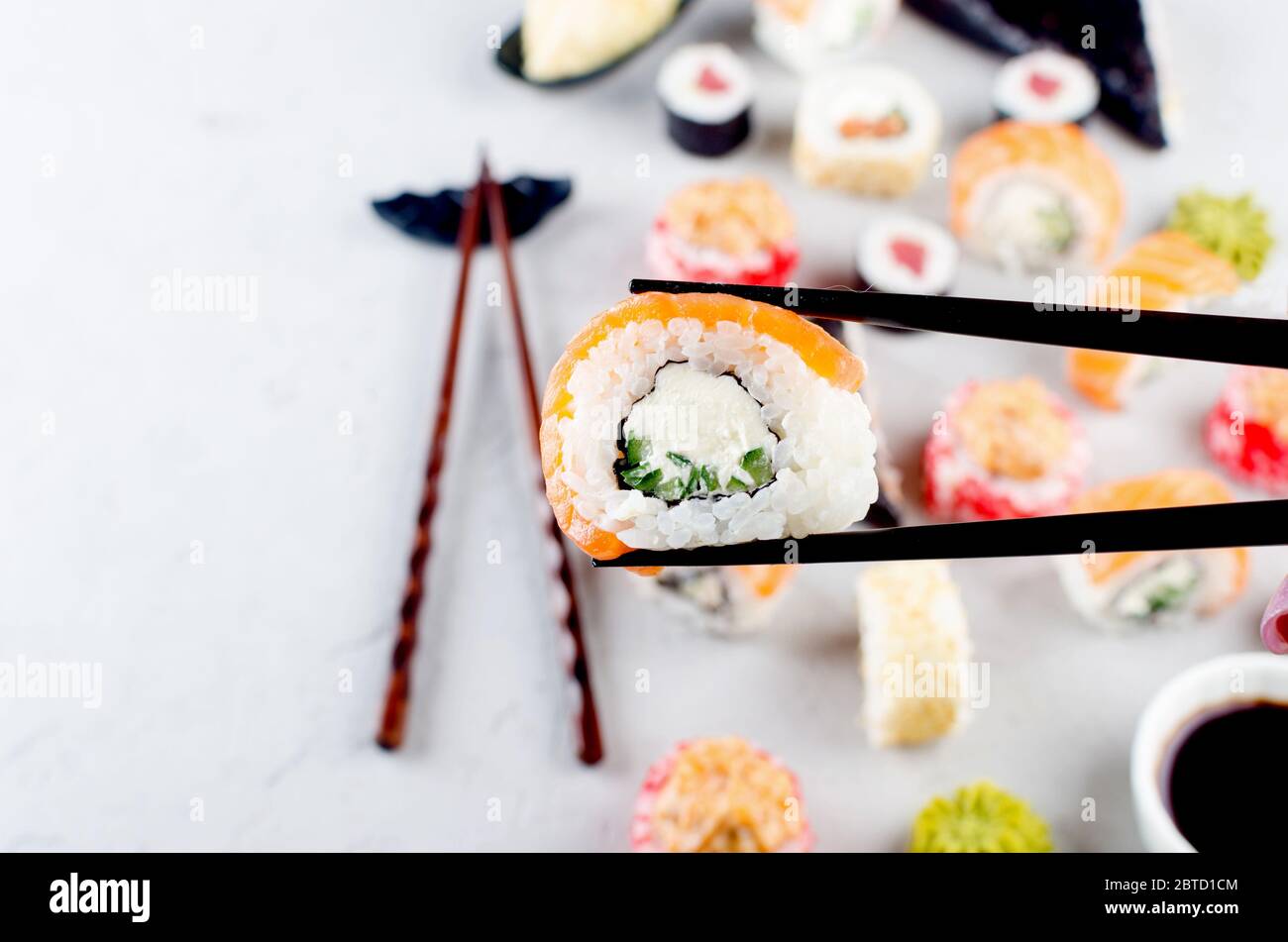 Nahaufnahme der Essstäbchen, die eine Portion Sushi-Rolle über dem Tisch mit verschiedenen Sushi, Sojasauce, Ingwer, Wasabi einnehmen. Sushi-Menü. Lieferservice Japanisch Stockfoto