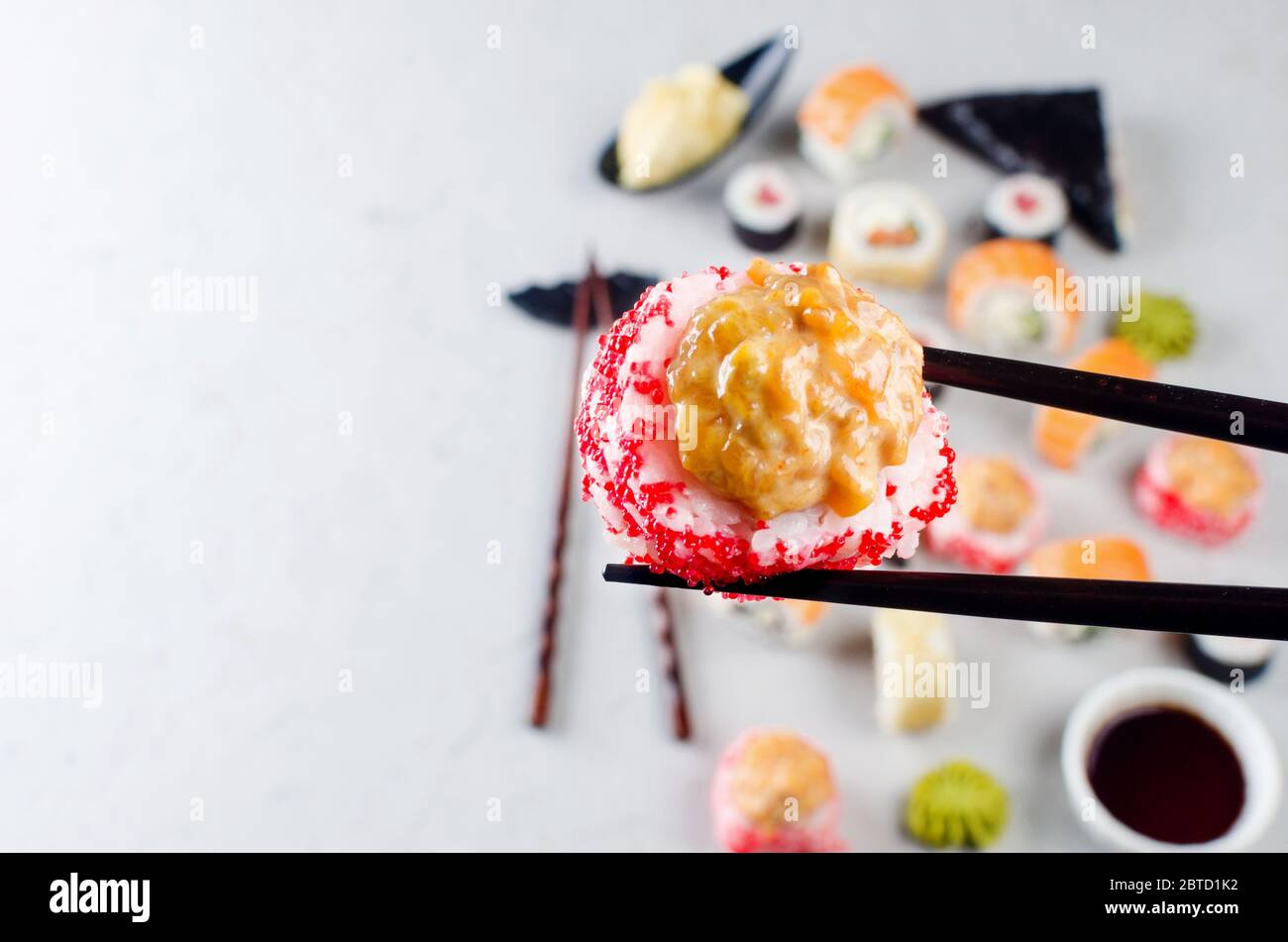 Nahaufnahme der Essstäbchen, die eine Portion Sushi-Rolle über dem Tisch mit verschiedenen Sushi, Sojasauce, Ingwer, Wasabi einnehmen. Sushi-Menü. Lieferservice Japanisch Stockfoto