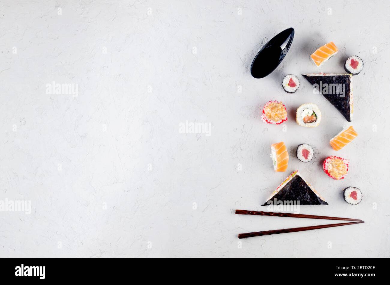 Verschiedene Sushi und Brötchen mit Sojasoße, Ingwer, Wasabi und Essstäbchen auf einem grauen Betontisch. Sushi-Menü. Lieferservice Japanisches Essen. Stockfoto