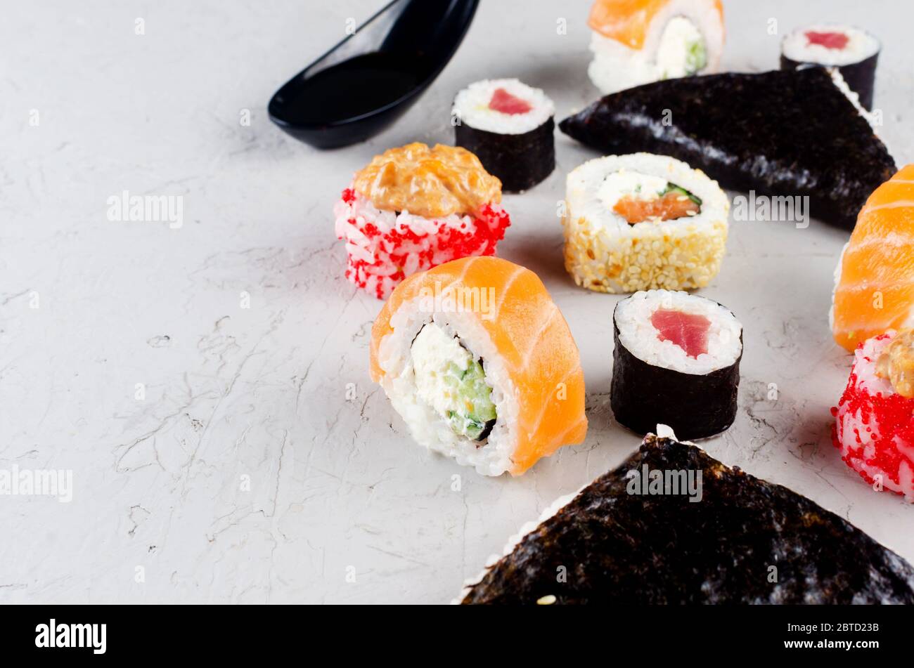 Verschiedene Sushi und Brötchen mit Sojasoße, Ingwer, Wasabi und Essstäbchen auf einem grauen Betontisch. Sushi-Menü. Lieferservice Japanisches Essen. Stockfoto