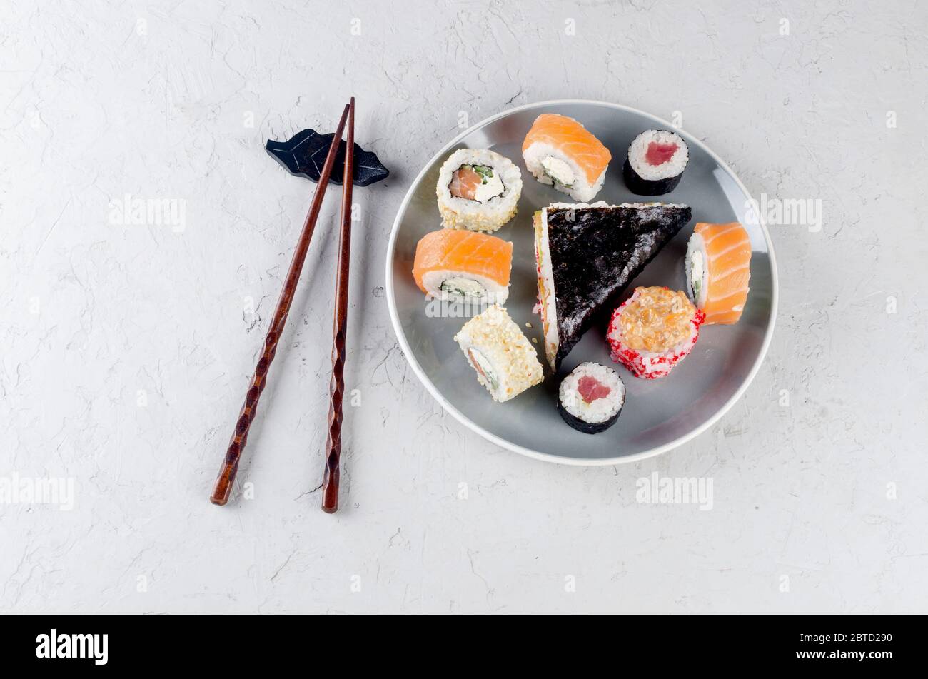 Verschiedene Sushi-Brötchen auf einem Teller und Sojasoße, Ingwer, Wasabi und Essstäbchen auf einem grauen Betontisch. Asiatische Speisekarte. Lieferservice Stockfoto