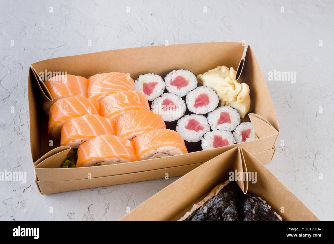 Leckere Sushi-Rollen in Einweg-Kraftpapier-Boxen, Sauce auf dunklem Tisch. Konzept Lieferservice Japan Lebensmittel in Öko-Container. Flaches Lay, Schablone Mocku Stockfoto