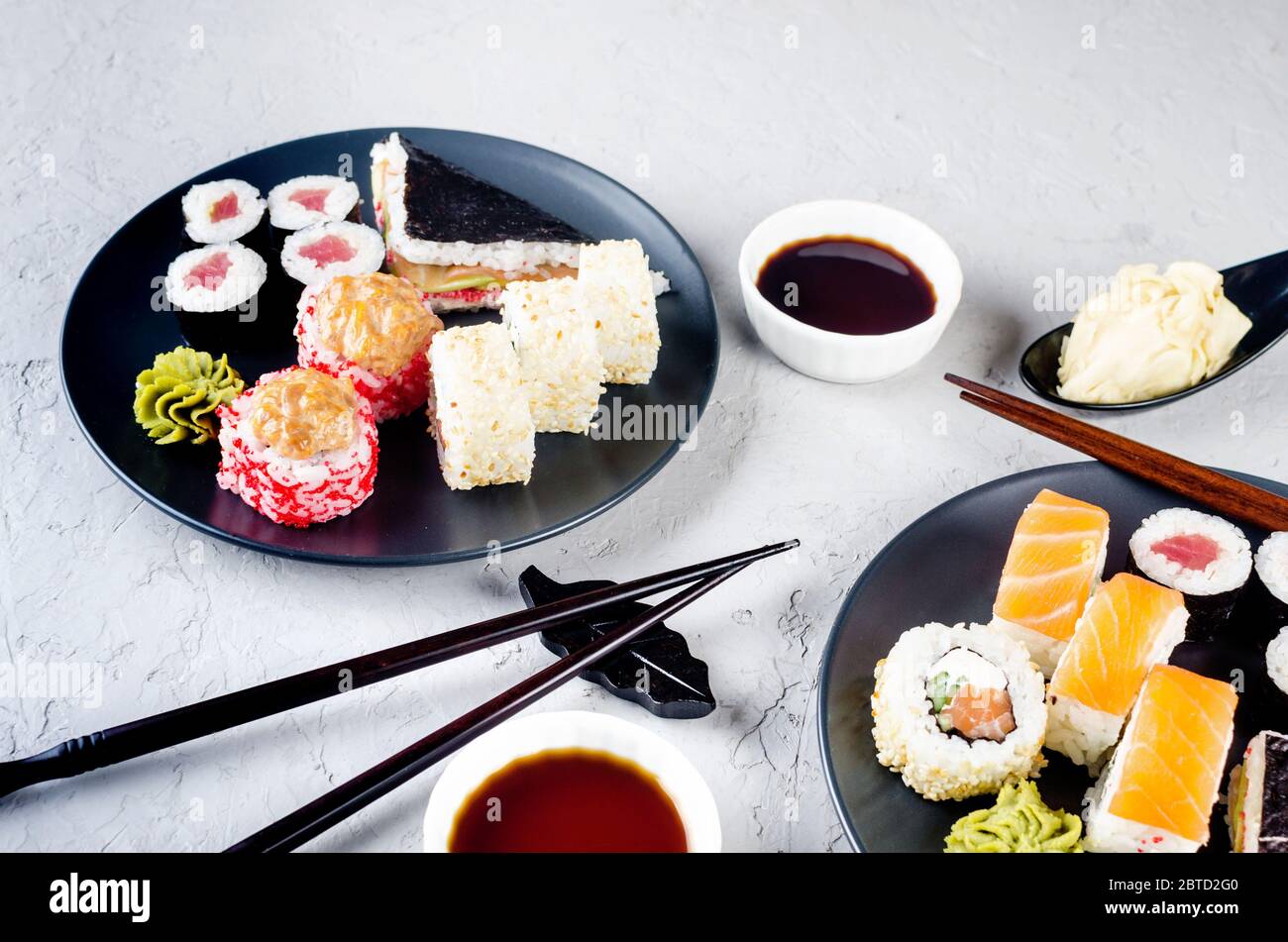 Verschiedene Sushi-Brötchen auf einem Teller und Sojasoße, Ingwer, Wasabi und Essstäbchen auf einem grauen Betontisch. Asiatische Speisekarte. Lieferservice Stockfoto