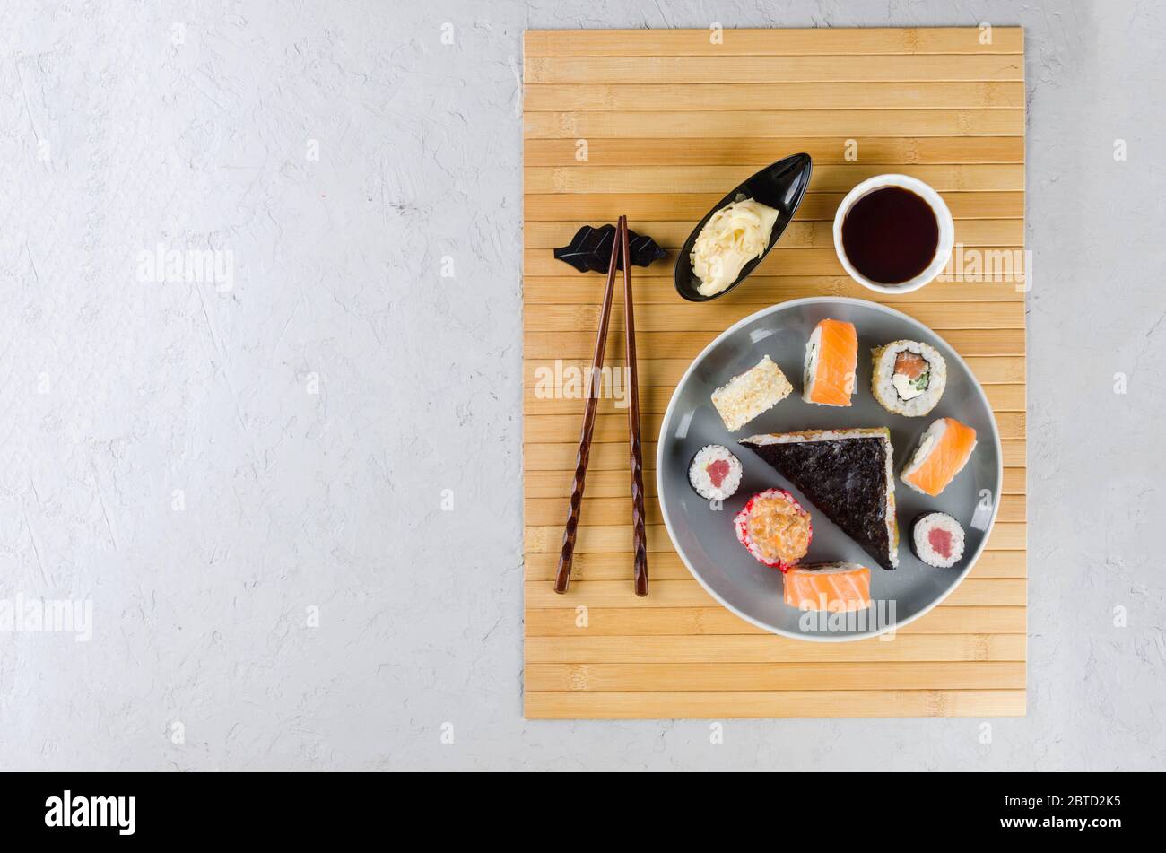 Verschiedene Sushi-Brötchen auf einem Teller und Sojasoße, Ingwer, Wasabi und Essstäbchen auf einem grauen Betontisch. Asiatische Speisekarte. Lieferservice Stockfoto
