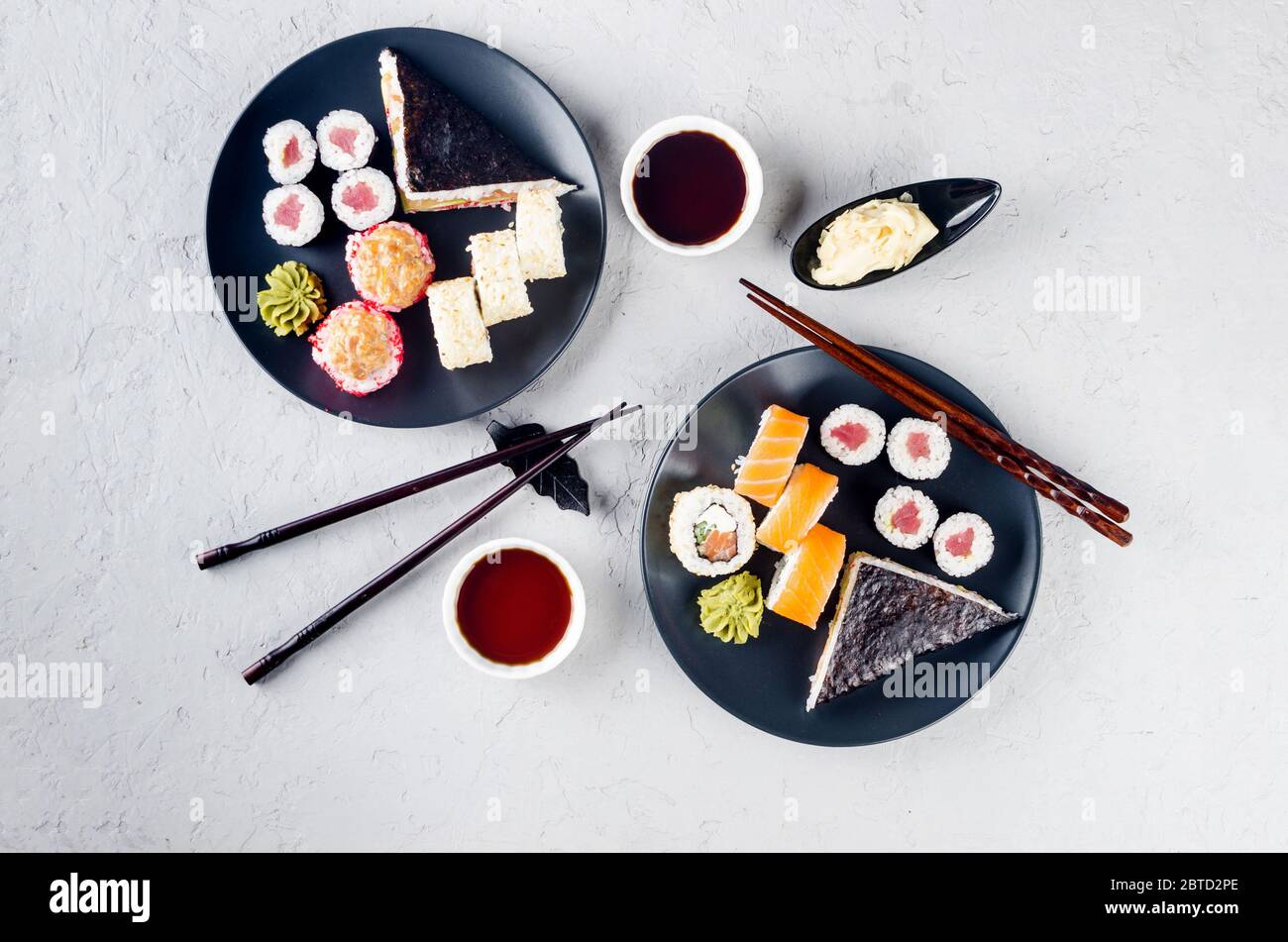 Verschiedene Sushi-Brötchen auf einem Teller und Sojasoße, Ingwer, Wasabi und Essstäbchen auf einem grauen Betontisch. Asiatische Speisekarte. Lieferservice Stockfoto